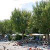Una spiaggia di ciottoli con alberi, tende e gommoni colorati.