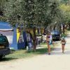 Due persone camminano lungo un sentiero in un campeggio con tende e auto parcheggiate.