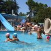 Una piscina con scivoli d'acqua, bambini che nuotano e persone che si rilassano.