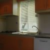 Cucina con fornelli a gas, lavandino, pensili arancioni e finestra con tende veneziane.