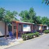 Esterno di un campeggio con bungalow, sedie a sdraio e ombra degli alberi.