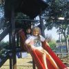 Due bambini scendono sorridenti da uno scivolo rosso al parco giochi.