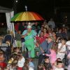Un clown con un ombrello colorato intrattiene un pubblico di bambini e adulti.