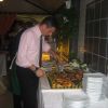 Uomo in camicia rosa che taglia una grande torta alla frutta su un tavolo da buffet.