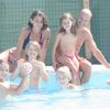 Gruppo di persone sorridenti in una piscina, con alcuni che giocano con una palla.