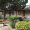 Una fila di bungalow con verande, tavoli bianchi e vegetazione circostante.