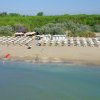 Spiaggia con ombrelloni e cabine, verde sullo sfondo.